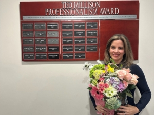 A woman holding a flower bouquet posing in front of a plaque board.