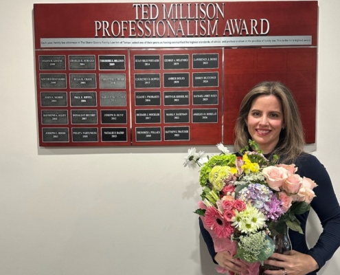 A woman holding a flower bouquet is posing in front of a plaque board.