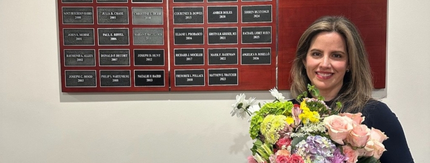 A woman holding a flower bouquet is posing in front of a plaque board.