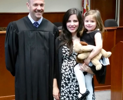 A man wearing judicial robes is standing in a courtroom with a woman who is holding a child.