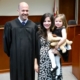 A man wearing judicial robes is standing in a courtroom with a woman who is holding a child.