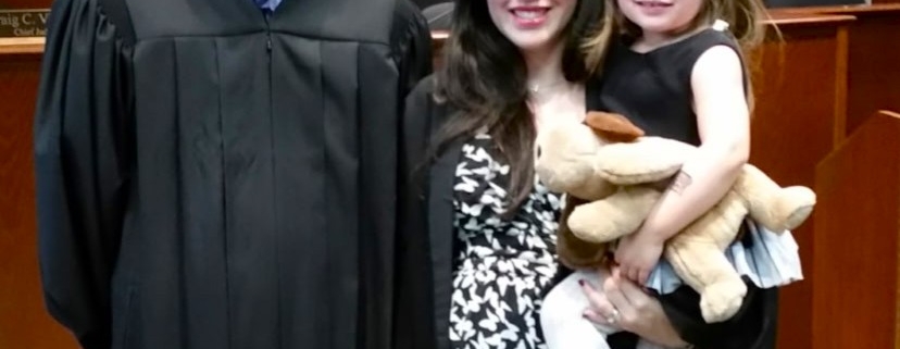 A man wearing judicial robes is standing in a courtroom with a woman who is holding a child.