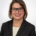 A woman with short brown hair is wearing glasses and business attire and smiling at the camera